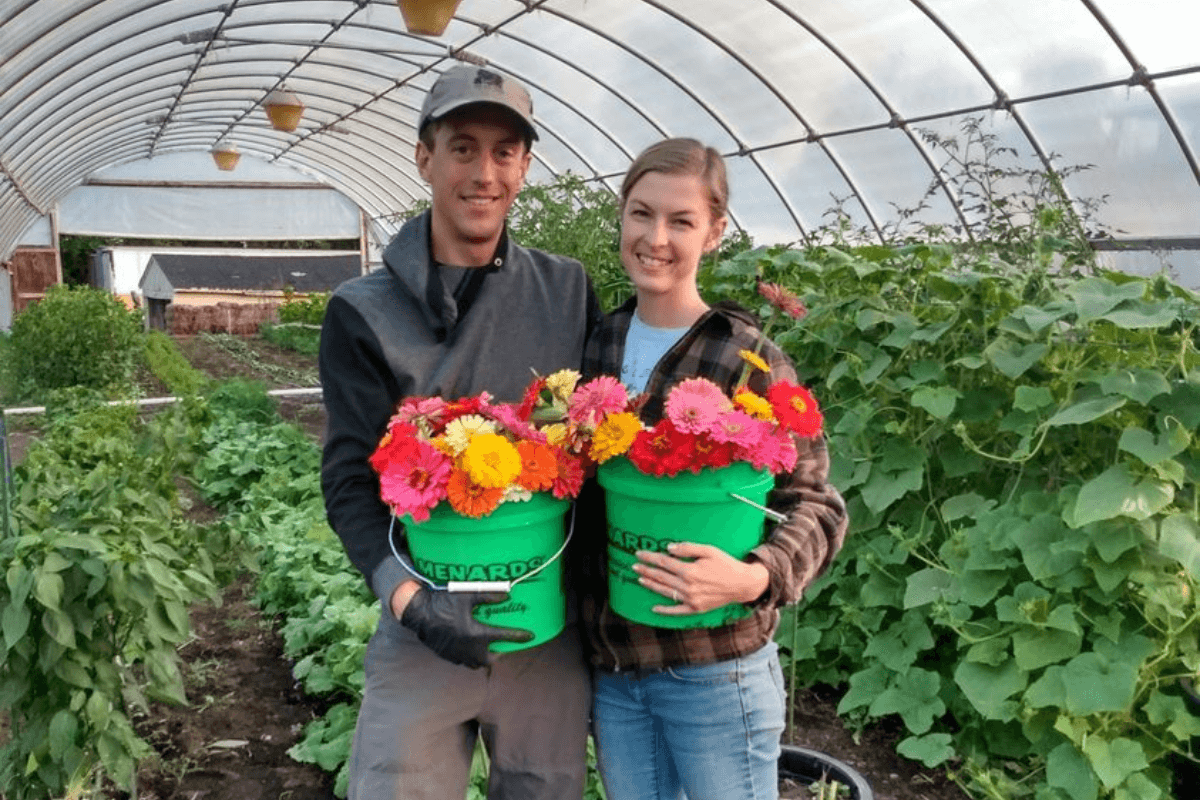 anna and robert merkt in greenhouse holding big buckets of brightly colored zinnias